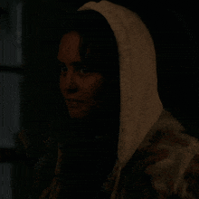 a woman wearing a white fur coat with a hood looks at the camera