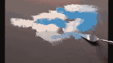 a palette knife is being used to spread blue and white paint on a canvas