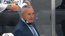 a man wearing a suit and tie is sitting in the stands watching a hockey game