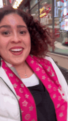 a woman wearing a white jacket and a pink scarf smiles for the camera
