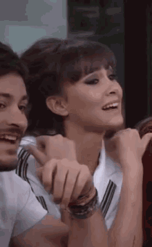 a man and a woman are sitting next to each other and the woman is smiling and pointing at the man .