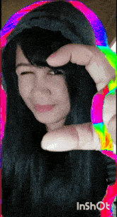 a woman is making a heart shape with her fingers while wearing a rainbow colored hoodie