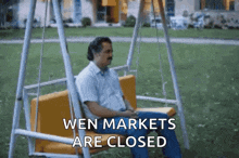 a man is sitting on a swing that says wen markets are closed