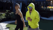 a man in a neon yellow hoodie is dancing with a woman in a black tank top