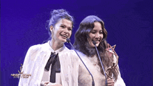 two women stand in front of microphones holding a trophy with a star in the middle
