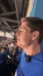 a man wearing a blue adidas shirt stands in a stadium