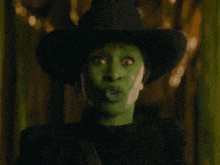 a witch with a green face is holding her finger to her lips