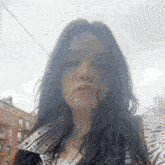 a woman with long dark hair is standing in front of a building smoking a cigarette .