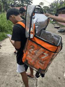 a man is carrying an orange bag that says 24/7 on it