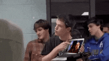 a group of young men are sitting around a table holding a laptop .