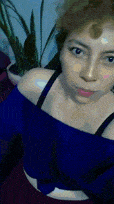 a woman in a blue off the shoulder top takes a selfie in front of a potted plant