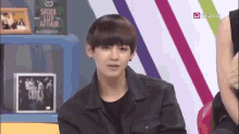 a young man in a black jacket is sitting in front of a sign that says skool love affair