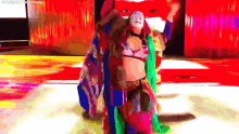 a woman in a colorful costume with a mask on her face is walking on a stage .