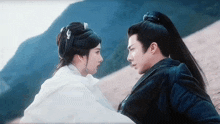 a man and a woman are looking at each other while sitting on a hill .