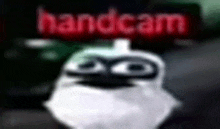 a cartoon character with a mask on his face is standing in front of a handcam sign .
