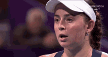 a woman wearing a white hat and earrings looks at the camera with a prime video arrow above her head