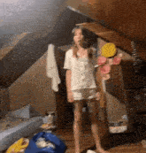 a young girl in a white shirt and shorts is standing in an attic .