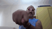 a man with a mustache wearing sunglasses and a blue tank top with a camel on it throws a fist