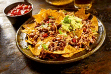 a plate of nachos with guacamole and salsa next to a bowl of salsa on a table .