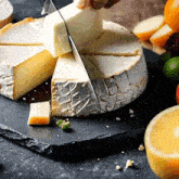 a person is cutting a piece of cheese on a black cutting board