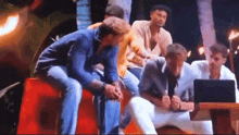 a group of men are sitting around a table with a laptop