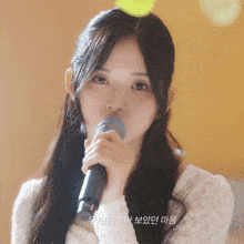 a girl singing into a microphone with korean writing on the bottom right