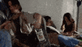 a man is holding a bottle of vodka in his hand while sitting next to a woman and another man .