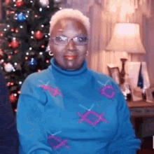 a woman in a blue sweater is smiling in front of a christmas tree