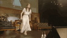 a woman in a white dress stands on a stage in front of a large screen