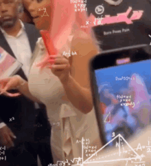 a woman with pink hair is standing in front of a cell phone with mathematical equations drawn on it