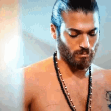 a shirtless man with a beard is wearing a necklace and looking down .