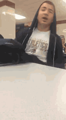 a man wearing a california athletics t-shirt is sitting at a table
