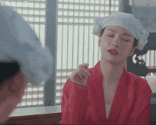 a woman wearing a red robe and a white towel on her head looks at herself in the mirror .
