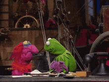 kermit the frog is sitting next to a purple flower