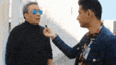 a man wearing sunglasses is being interviewed by a man wearing a name tag that says ' alonso ' on it