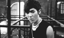 a black and white photo of a young man wearing a necklace and a sleeveless shirt .