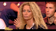 a woman with blonde curly hair is sitting in front of a star academy sign