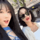 two women wearing sunglasses are standing next to each other on a sidewalk .