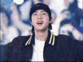 a man wearing a baseball cap and a jacket is standing in front of a crowd .