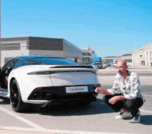 a man is squatting down in front of a white car that says car in wait on the back