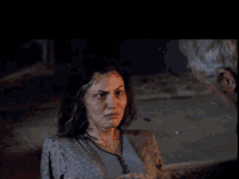 a woman with a scar on her face stands in the dark