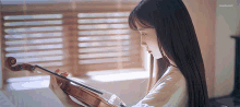 a woman is holding a violin in front of a window .