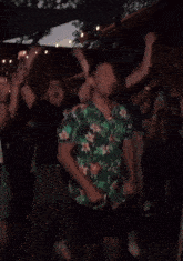 a man wearing a green floral shirt is dancing in a crowd