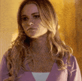 a woman with long blonde hair is wearing a purple sweater and looking at the camera .