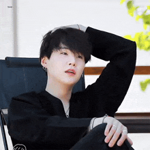 a young man in a black jacket is sitting in a chair with his hand on his head .