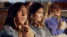 a group of young people are sitting in a car and one of them is pointing at his face .