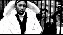 a black and white photo of a man in a fur coat standing in front of a crowd .