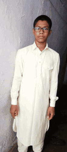 a young boy wearing glasses and a white shirt is standing in front of a wall