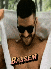 a shirtless man wearing sunglasses has the name bassem written on his chest