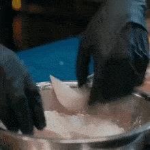 a person wearing black gloves is mixing ingredients in a metal bowl with a spatula .